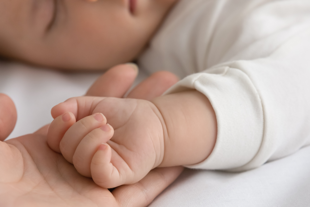 Dettaglio della manina di un neonato nel palmo di un adulto, simbolo di sensibilità e bisogno di protezione