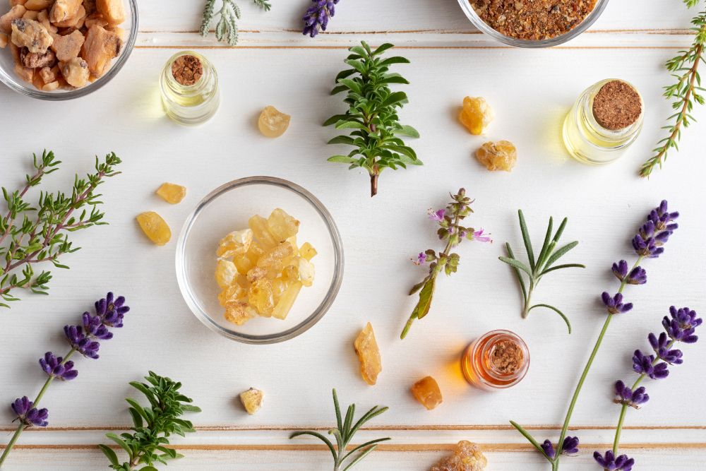 Flaconcini con oli essenziali circondati da erbe fresche e fiori per l'aromaterapia
