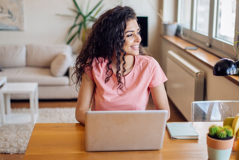 Donna sorridente al notebook in un ufficio domestico, simbolo di soddisfazione e benessere grazie all'aromaterapia durante il lavoro