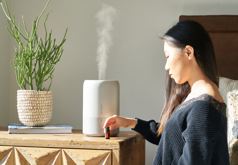 Una donna versa olio essenziale in un diffusore di aromi come parte della preparazione a una serata tranquilla.
